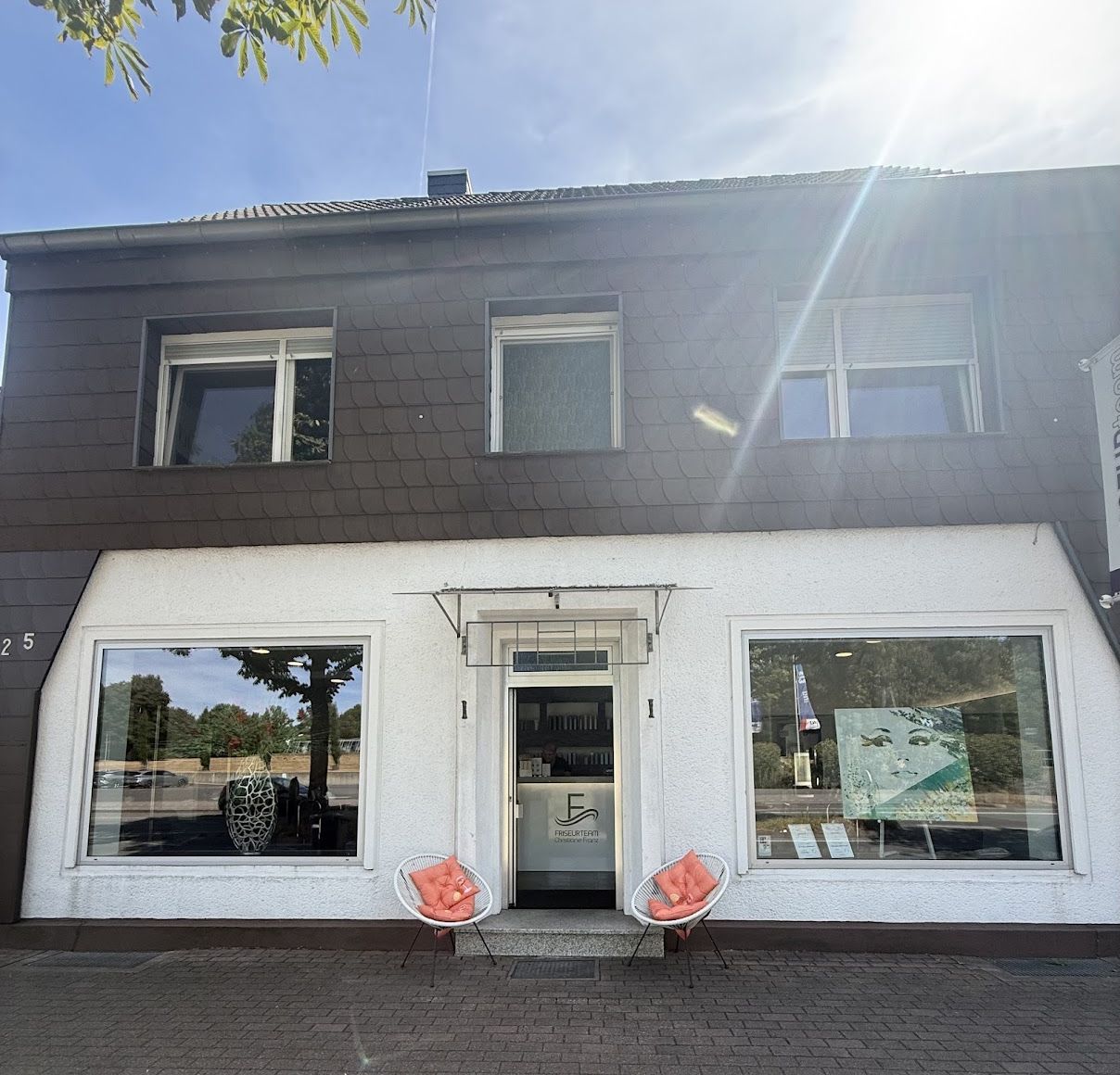 Der Salon von außen: weißes Ladenlokal mit Friseurteam-Logo an der Eingangstür